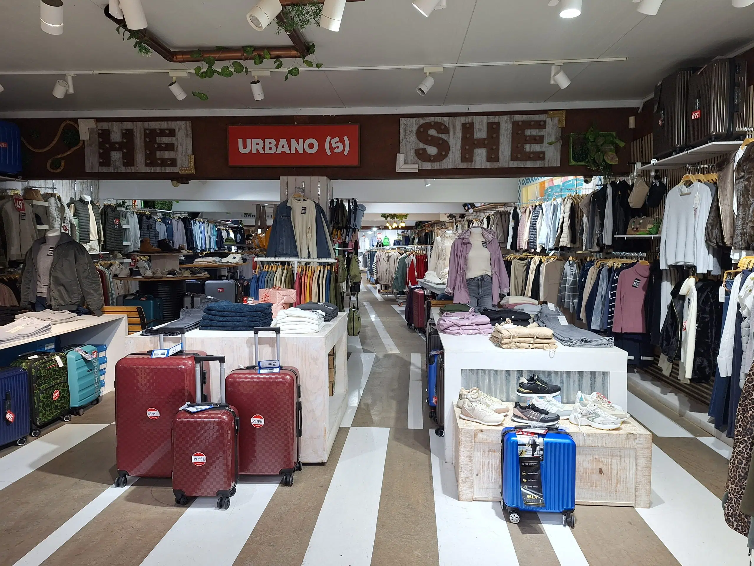 Interiör av en klädbutik med kläder och resväskor på display.