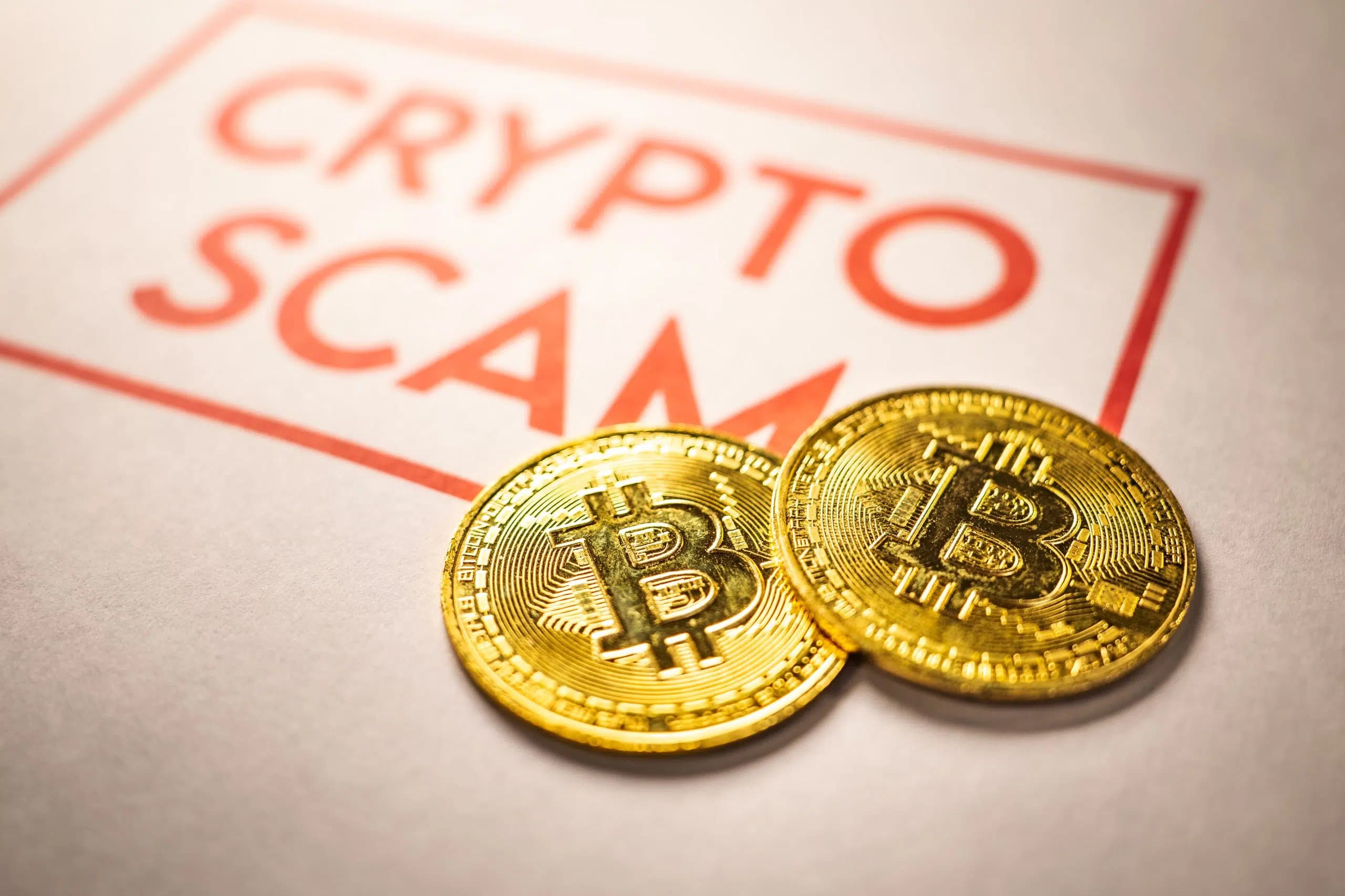 Två Bitcoin-mynt på ett papper med texten 'Crypto Scam'.